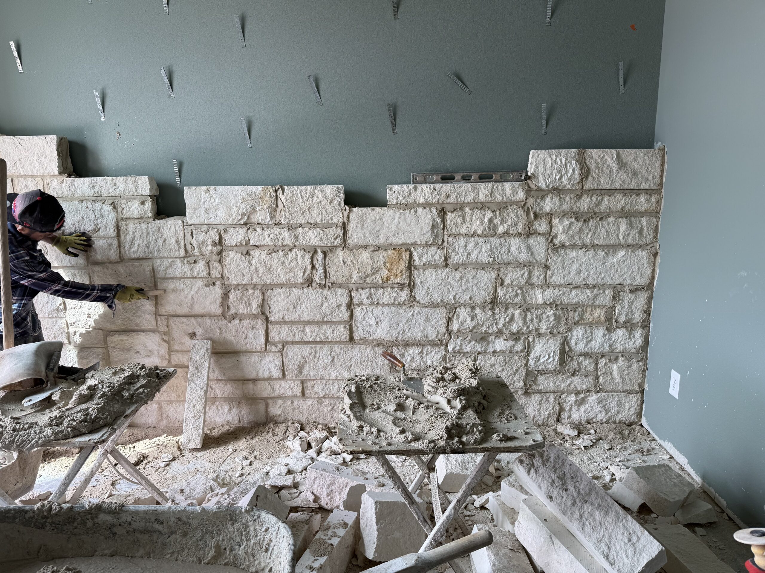 Mason installing natural stone veneer on an interior accent wall for a residential renovation.